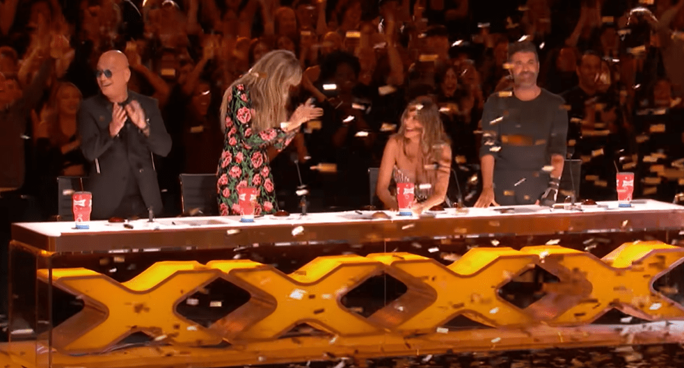 The judges' matching Xs on the front of the Judges' desk and above the stage turn to gold